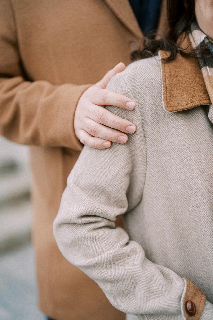 Close-up of a person wearing a beige coat with a hand resting gently on their shoulder, demonstrating warmth and companionship.