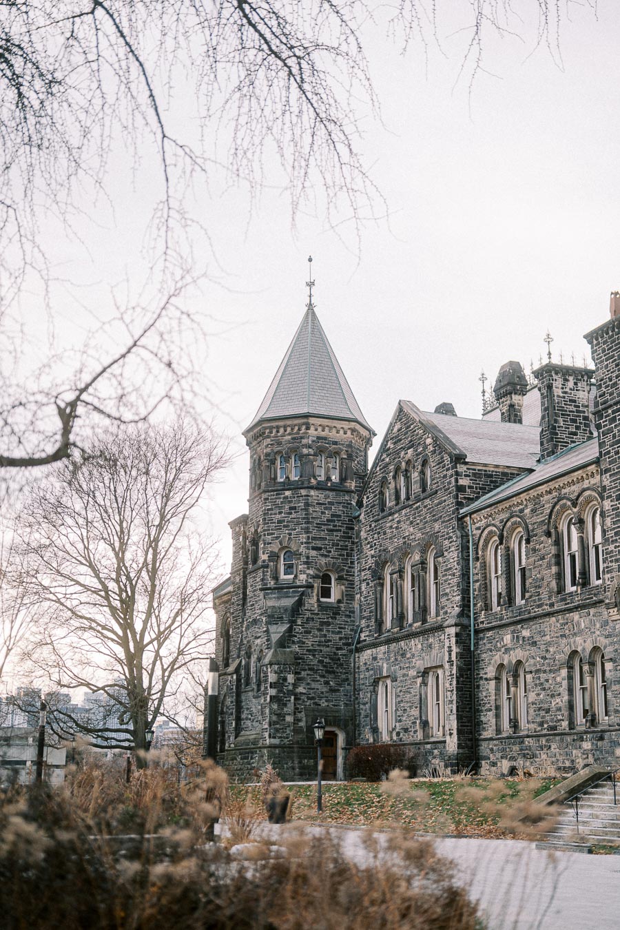 Medieval-style stone building with a turret, surrounded by bare winter trees and overcast sky.