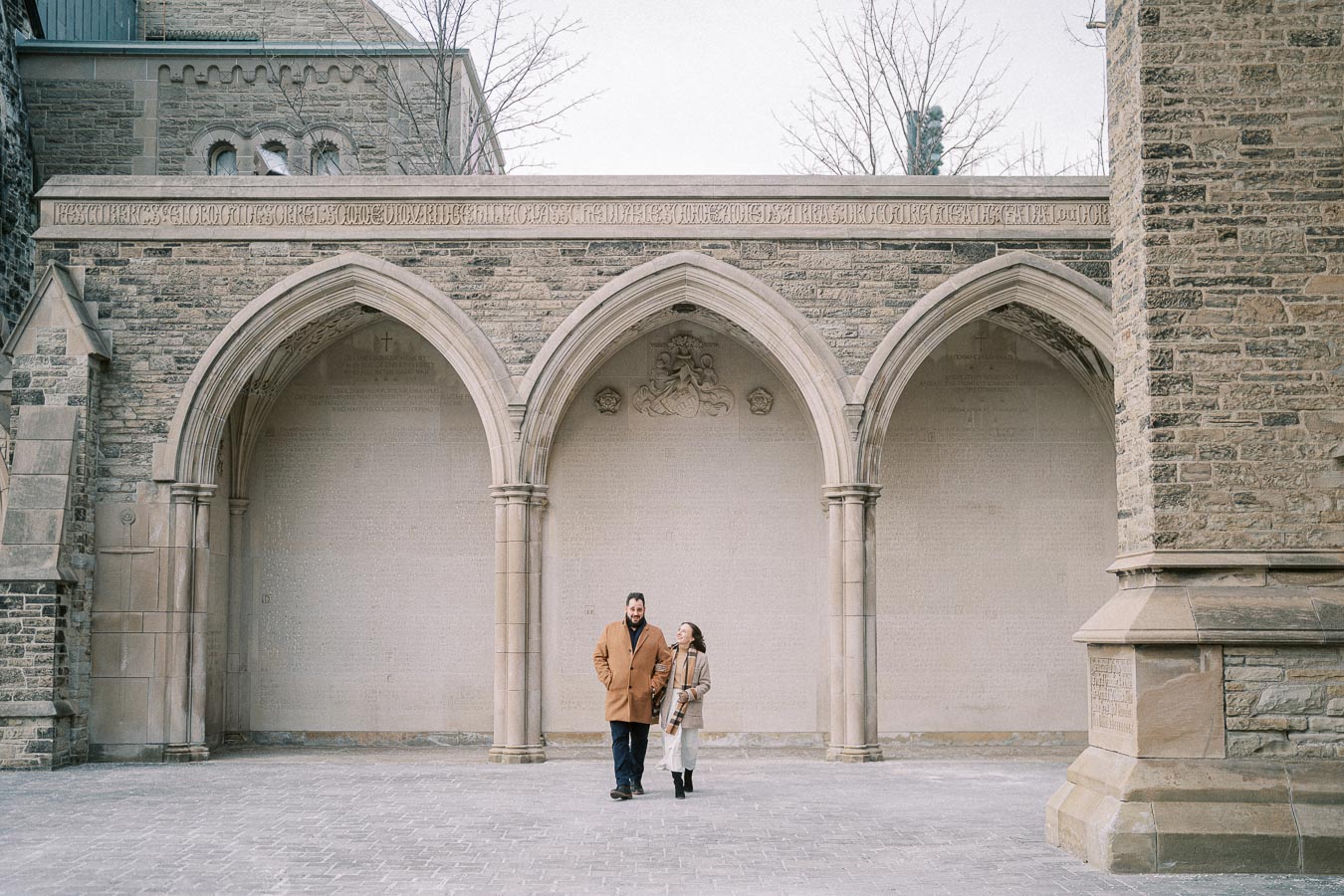 A couple walks together under historic stone archways.