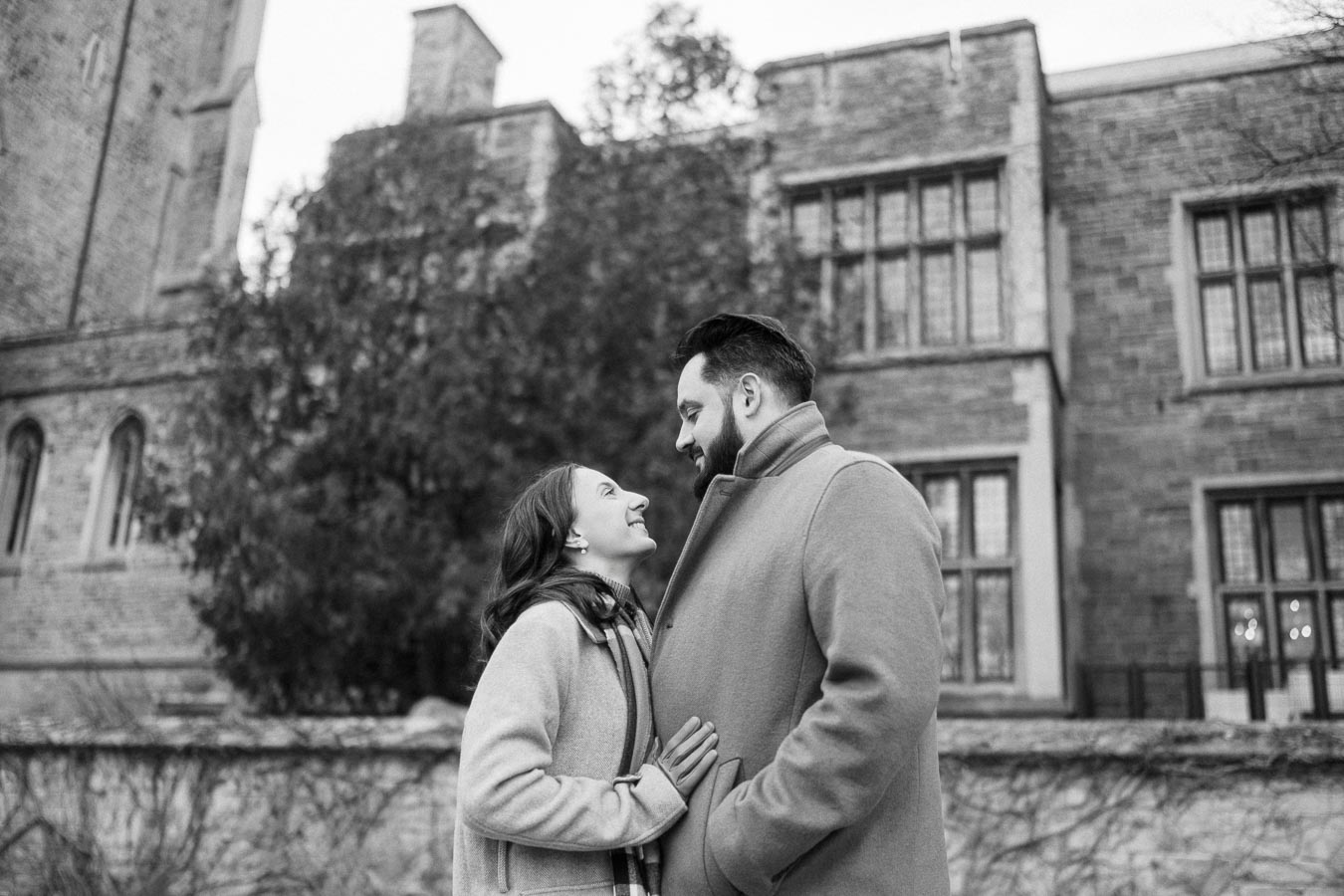 A happy couple gazing into each other's eyes, standing outside a historic brick building on a winter day.