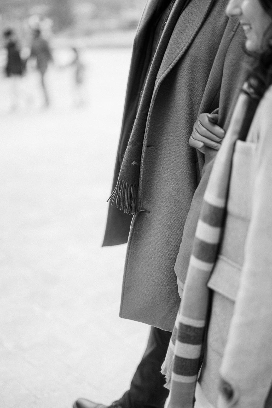 A grayscale photo of two people walking close together, wearing winter coats and scarves, with one person holding onto the other's arm, creating a warm, cozy atmosphere.