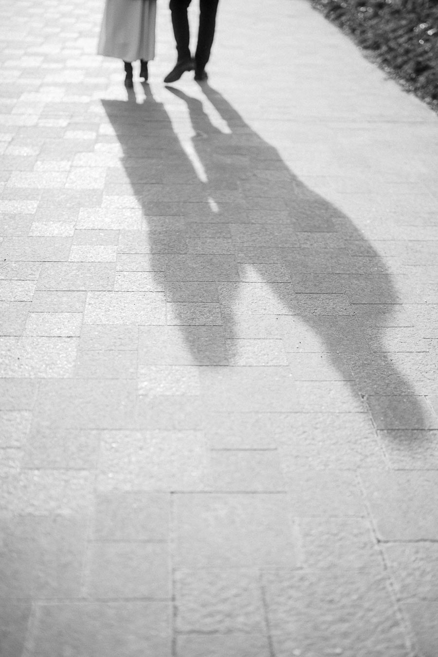 Silhouettes of a couple walking arm in arm on a sunlit brick pathway, casting long shadows.