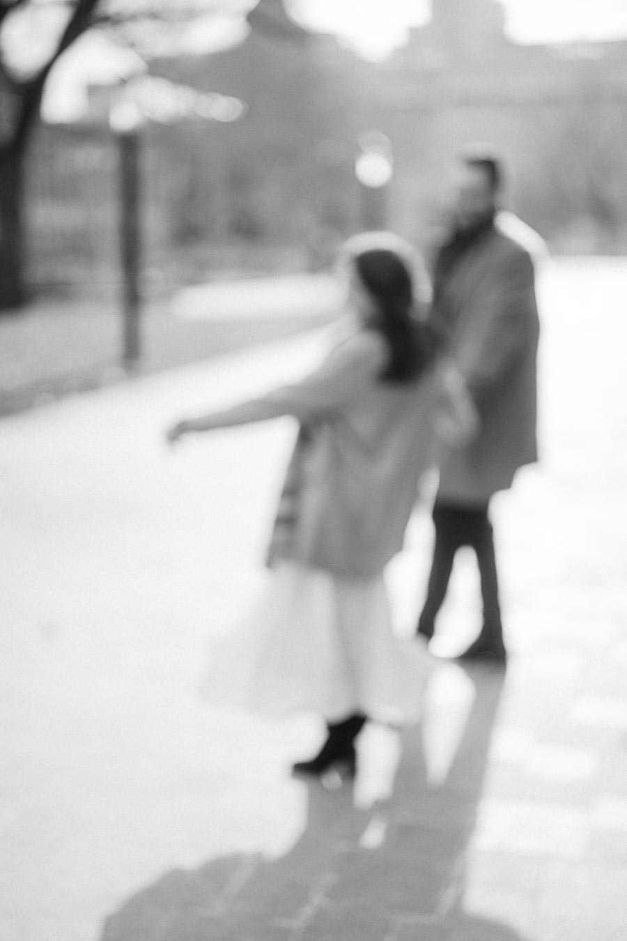 Blurred black and white photo of two people walking outdoors on a sunny day, surrounded by trees in a park setting.