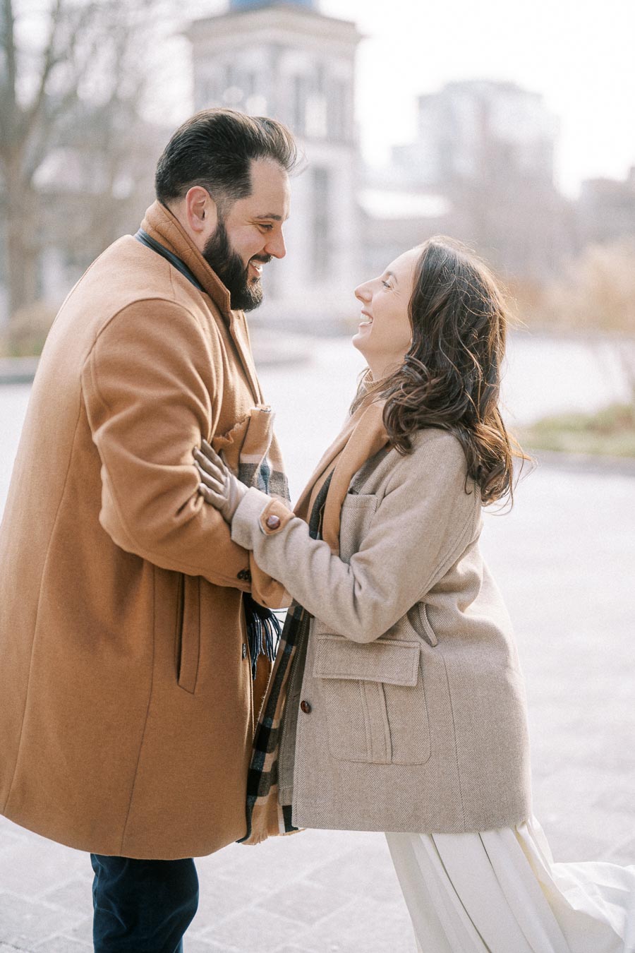 A happy couple warmly dressed in coats sharing a joyful moment outdoors during daytime.