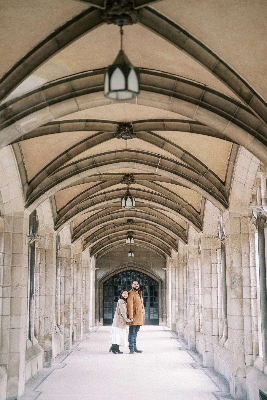 Couple standing in a beautiful, historic archway with stone walls and gothic architecture, highlighting an elegant and romantic atmosphere.