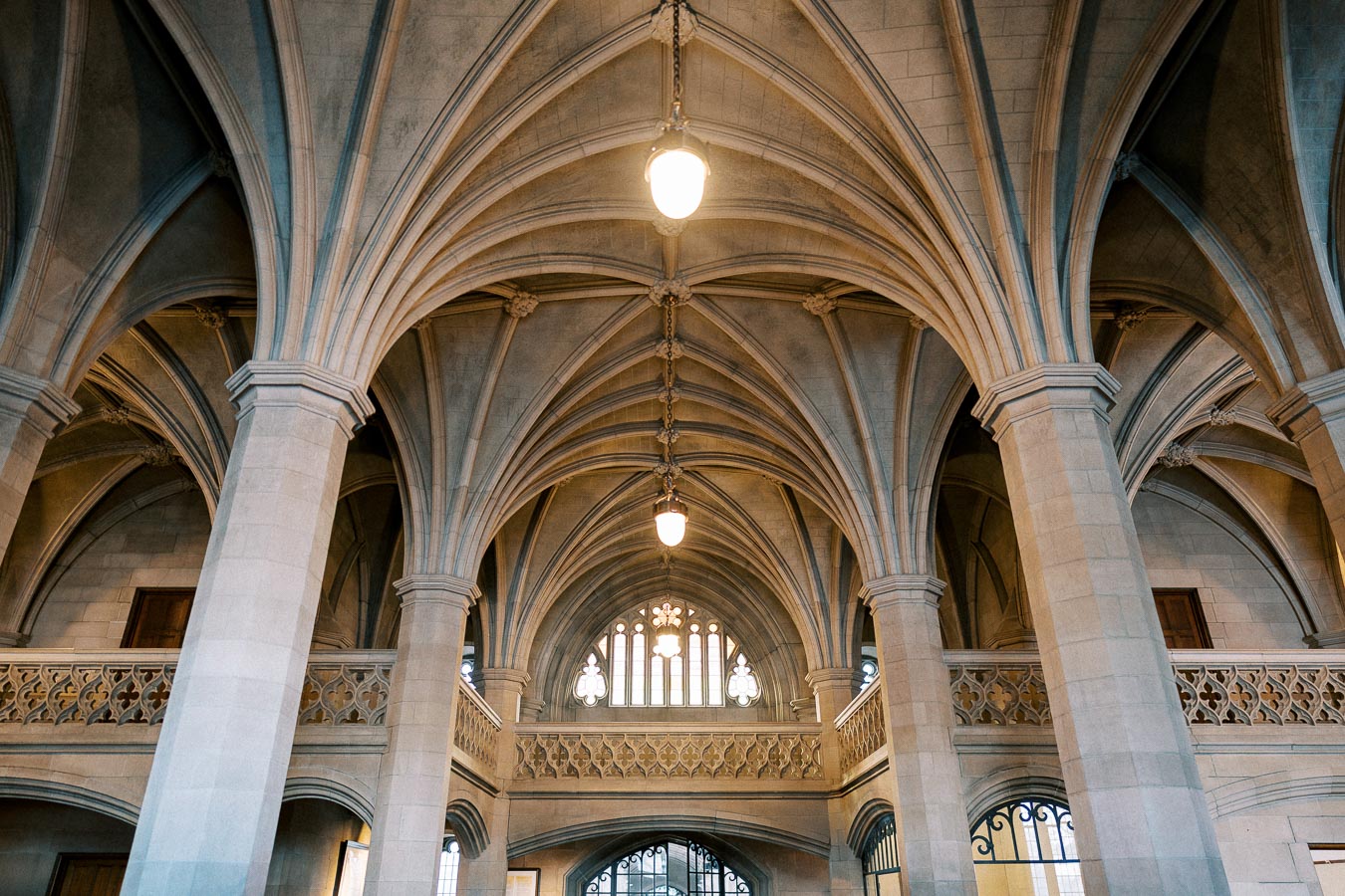 Grand Gothic architecture interior featuring vaulted ceilings with intricate stone arches and columns lit by hanging lights.