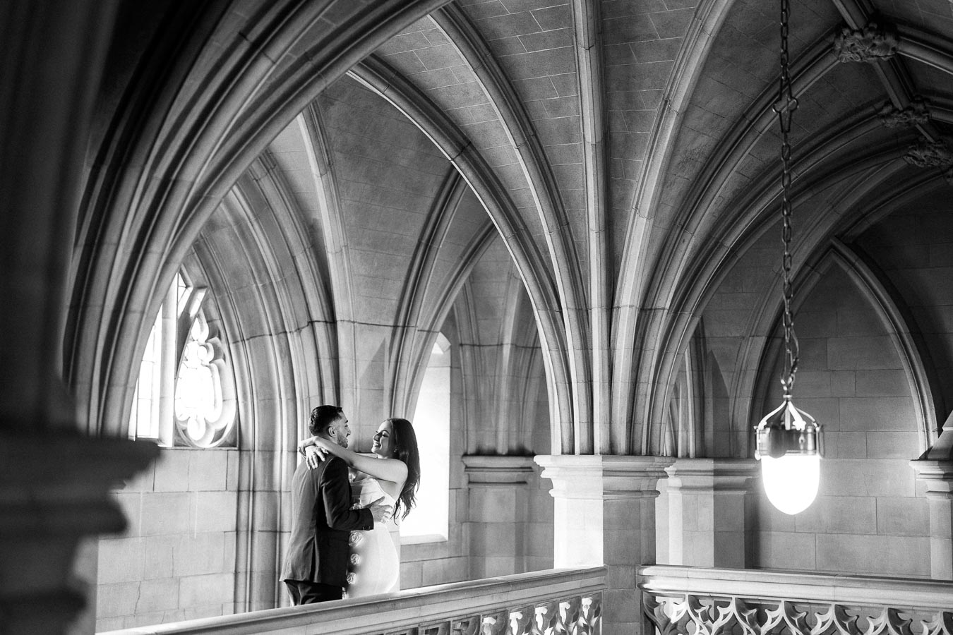 A couple embracing in a historic building with Gothic architectural elements, featuring ornate stone arches and soft