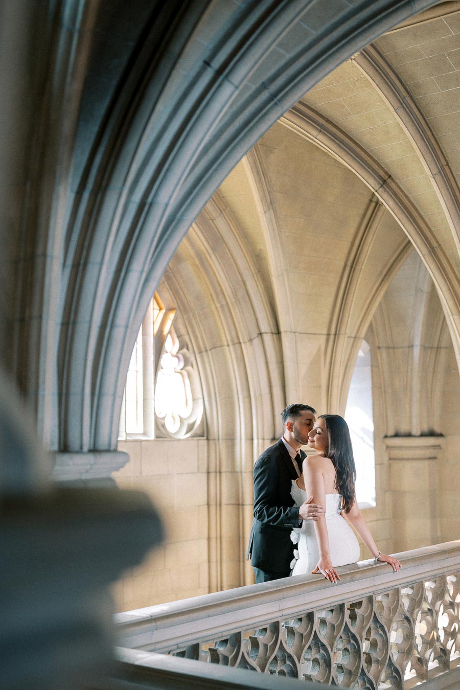 A couple embraces romantically in a Gothic-style architectural setting, featuring elegant stone arches and intricate
