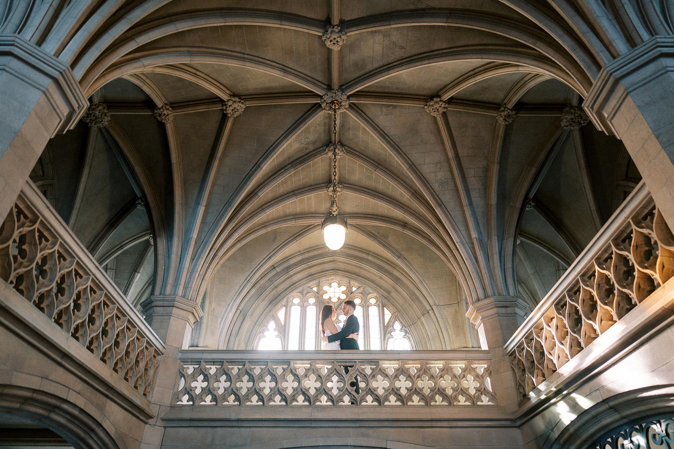 A couple standing on a balcony inside a grand gothic-style cathedral with intricate stonework and high vaulted ceilings,