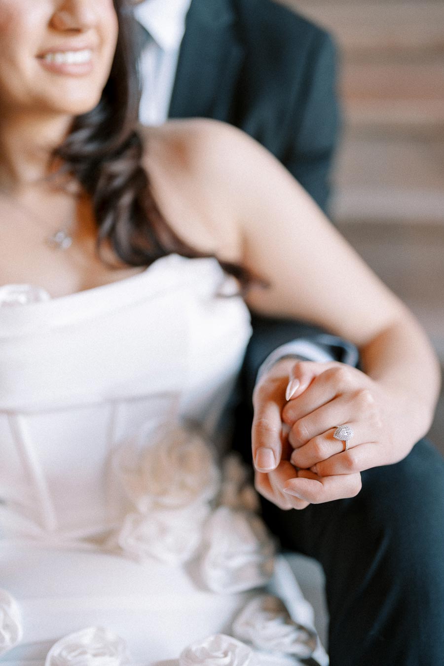 A bride in a white wedding dress holding hands with her partner, showcasing an elegant engagement ring.