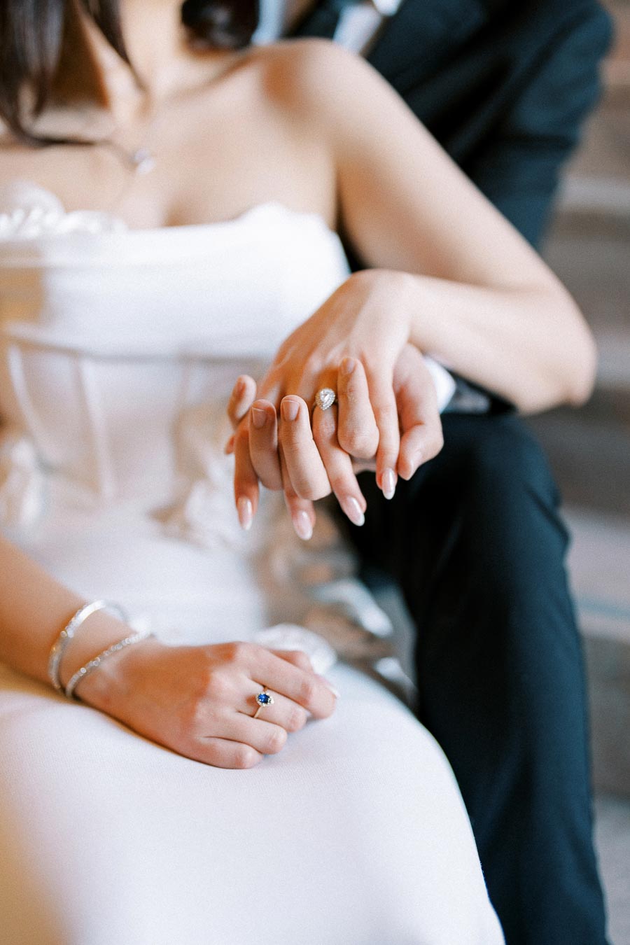 Elegant bride and groom holding hands with wedding rings, showcasing a romantic and intimate moment in wedding attire.