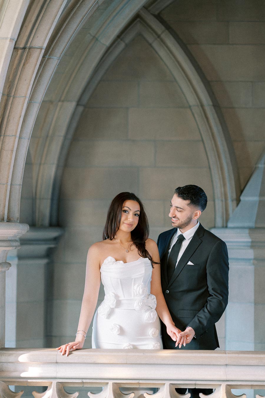 Elegant couple in formal attire posing in a beautifully arched architectural setting, showcasing a classic and romantic