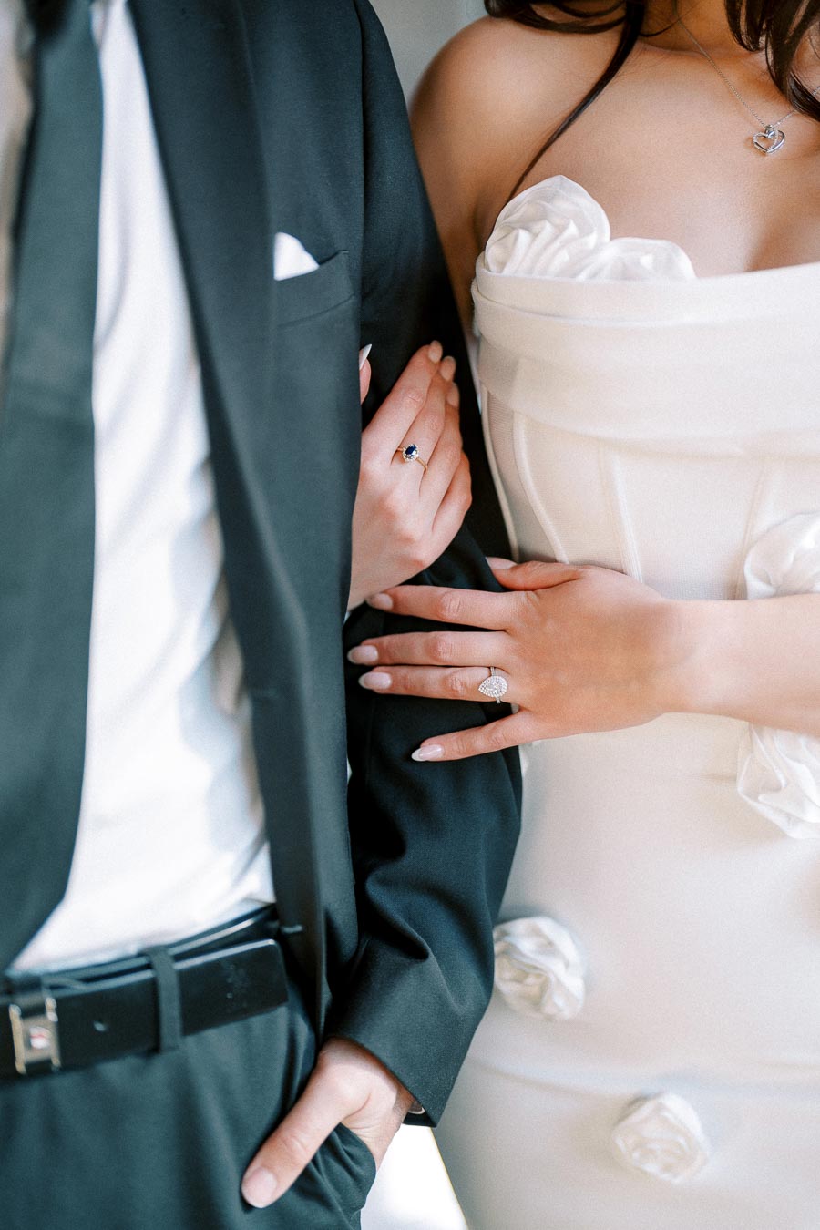 A bride in a white wedding dress holds her groom's arm, wearing an elegant diamond engagement ring, highlighting a romantic