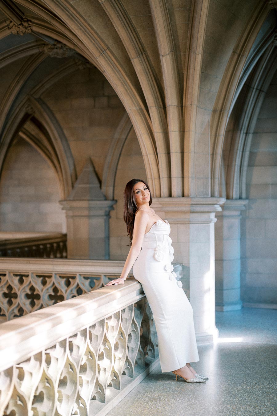 Elegant woman in a white dress posing in a historic stone archway, showcasing intricate architecture with ornamental