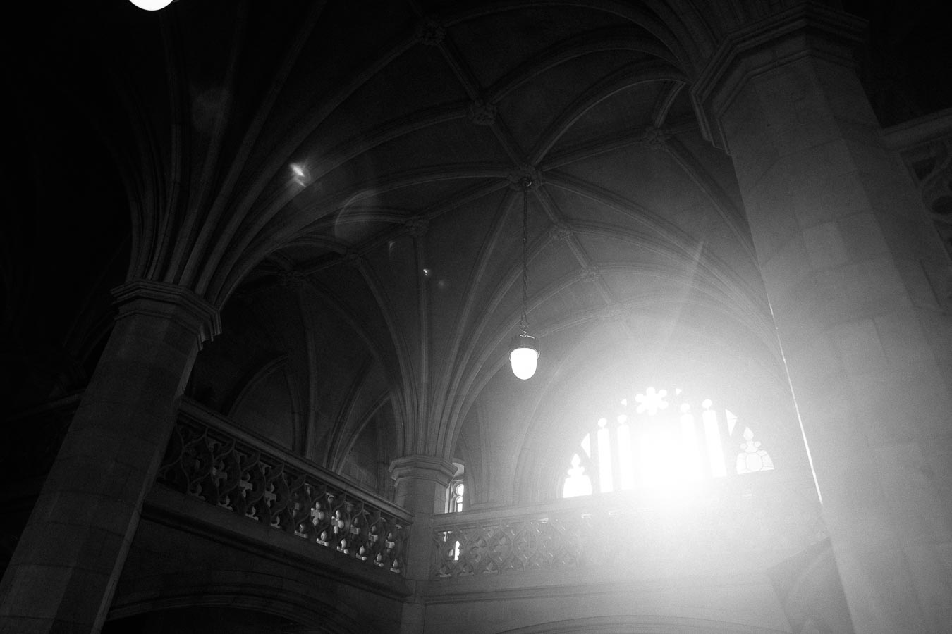 Sunlight streaming through the stained glass window of a Gothic cathedral, highlighting intricate vaulted ceiling and stone