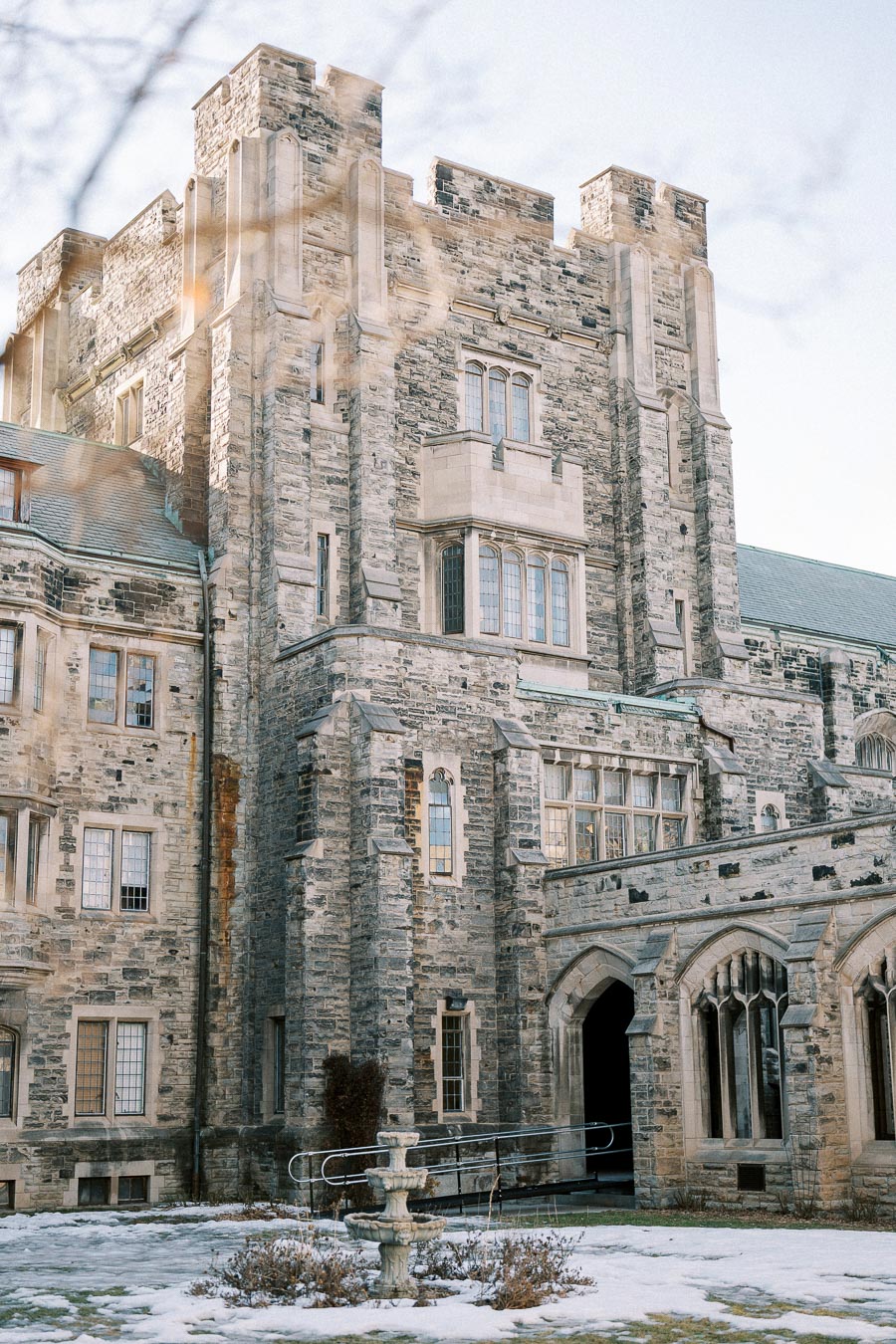 Medieval-style stone building with arched windows and a snow-covered courtyard, featuring a central water fountain, under a