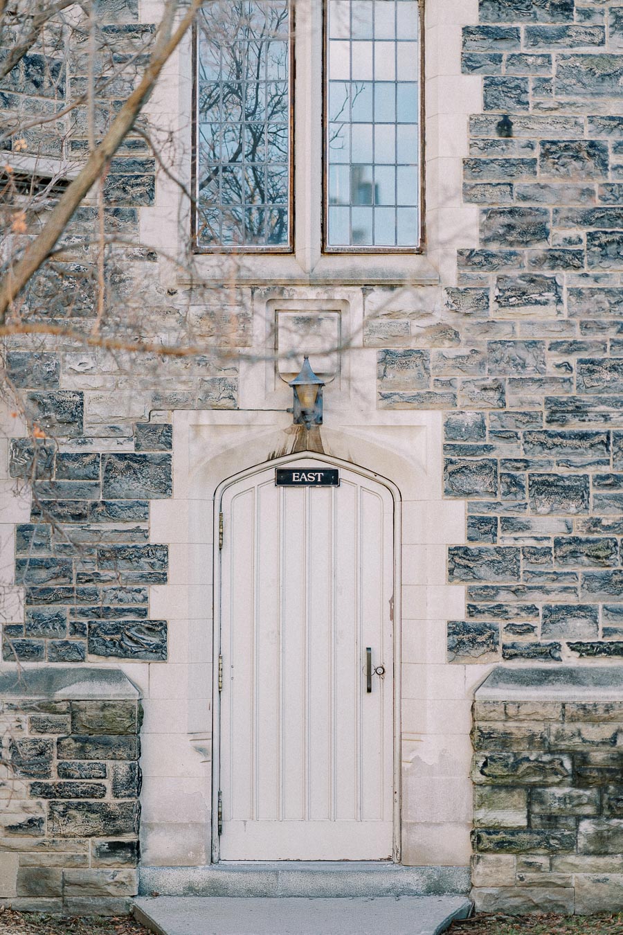 Vintage stone building featuring an arched wooden door marked 'East', with intricate windows and a classic outdoor lamp