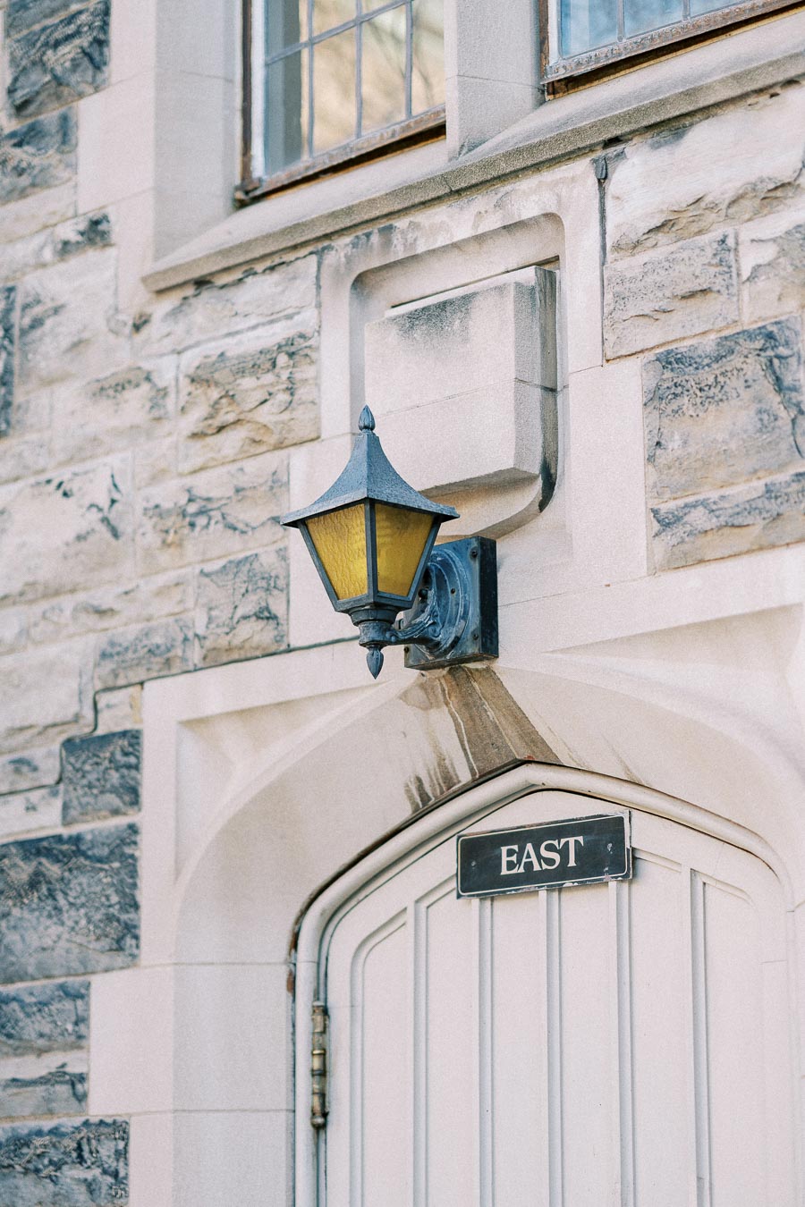 Close-up of a vintage lantern mounted on a stone wall above a wooden door labeled 'East' in an historic building.