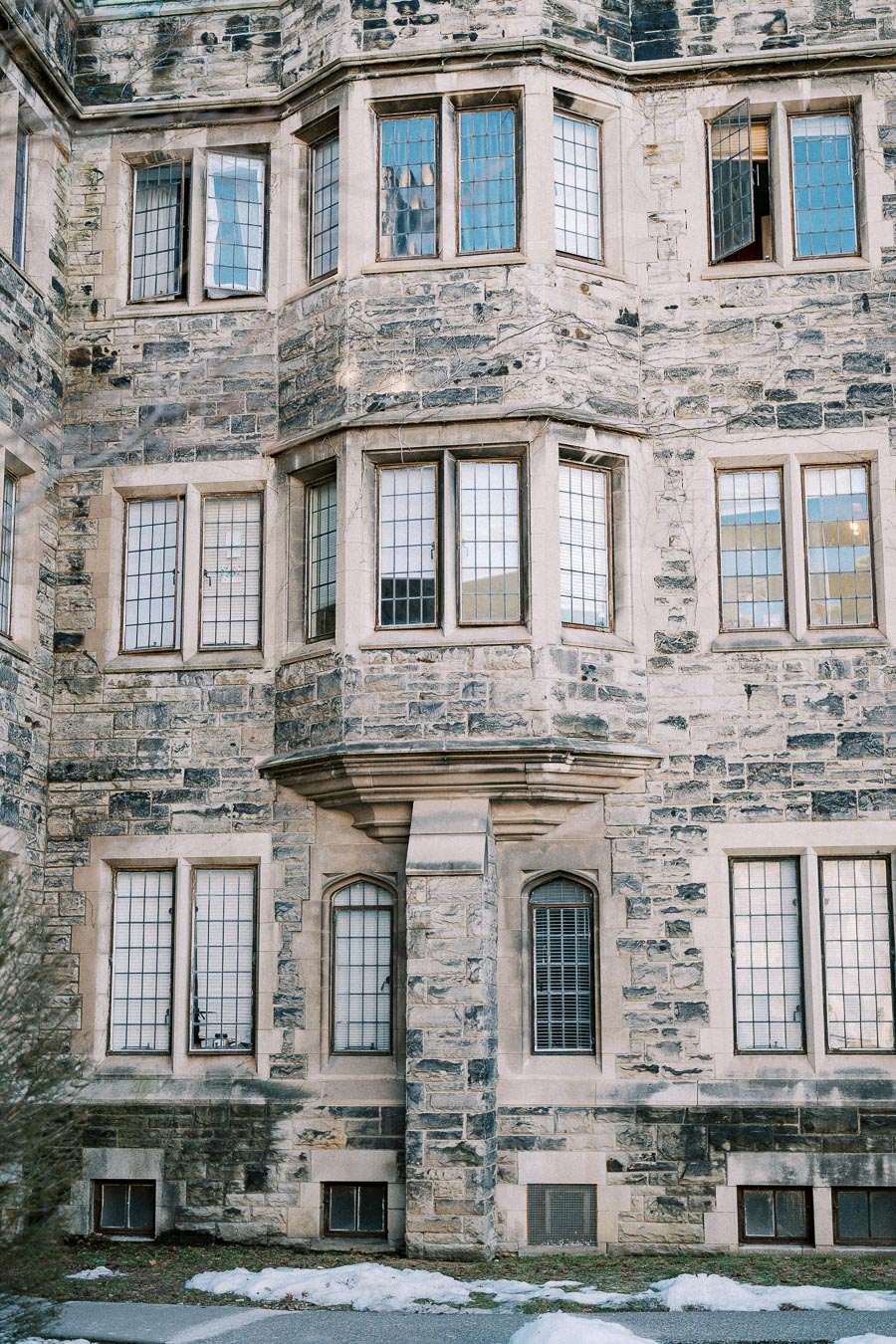 Stone facade of a historic building with multiple leaded glass windows, showcasing Gothic architectural elements, surrounded