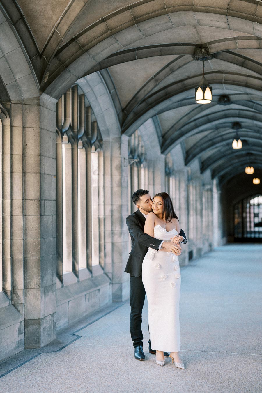 A couple embracing in a romantic corridor with Gothic-style architecture, soft lighting, and elegant archways.