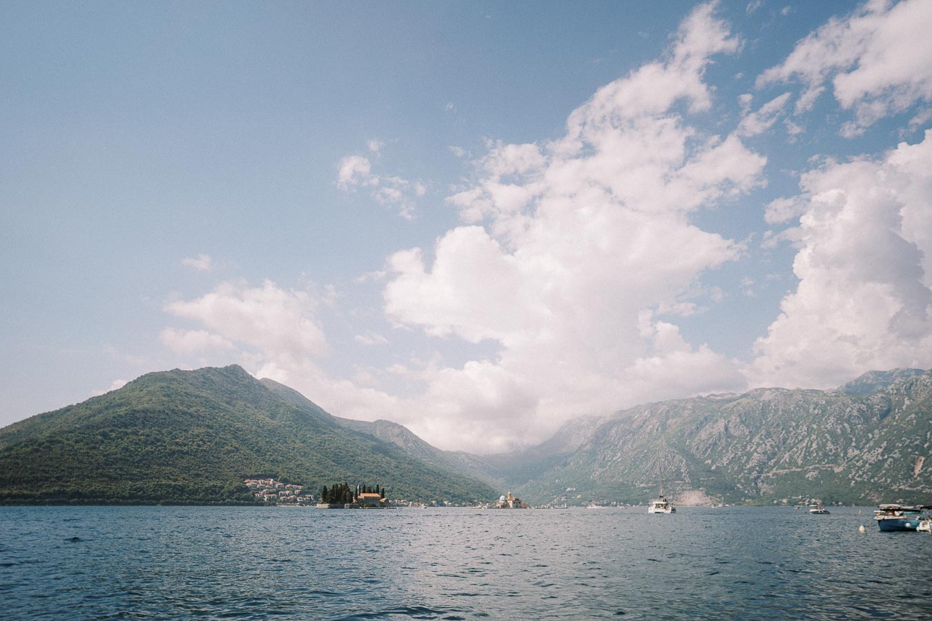 Scenic view of a tranquil bay with boats, surrounded by lush green mountains under a partly cloudy sky.