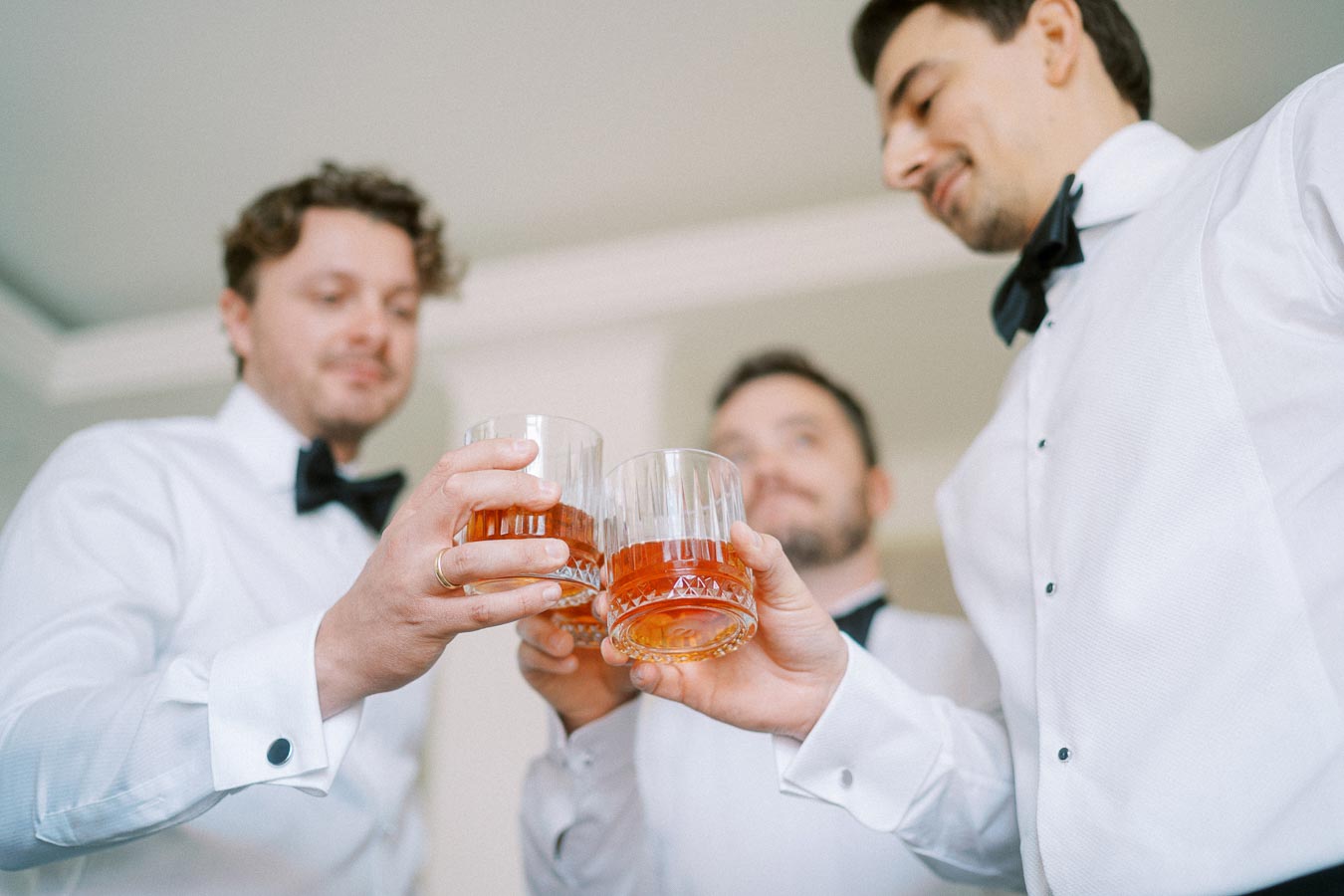 Three men in formal attire toasting with glasses of whiskey, celebrating a special occasion in a bright room.