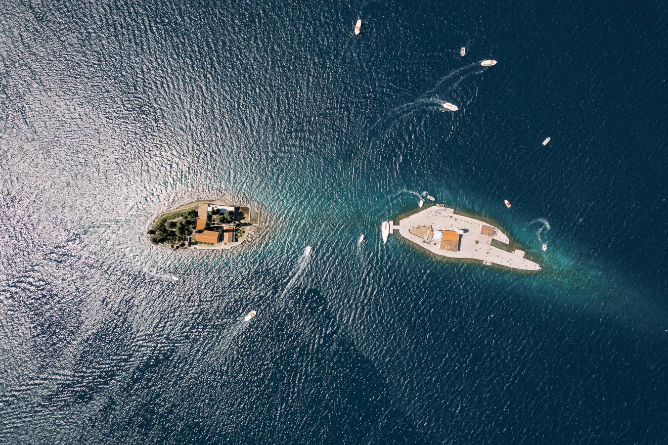Aerial view of two small islands surrounded by deep blue sea with several boats navigating the waters, showcasing vibrant marine life and scenic beauty.
