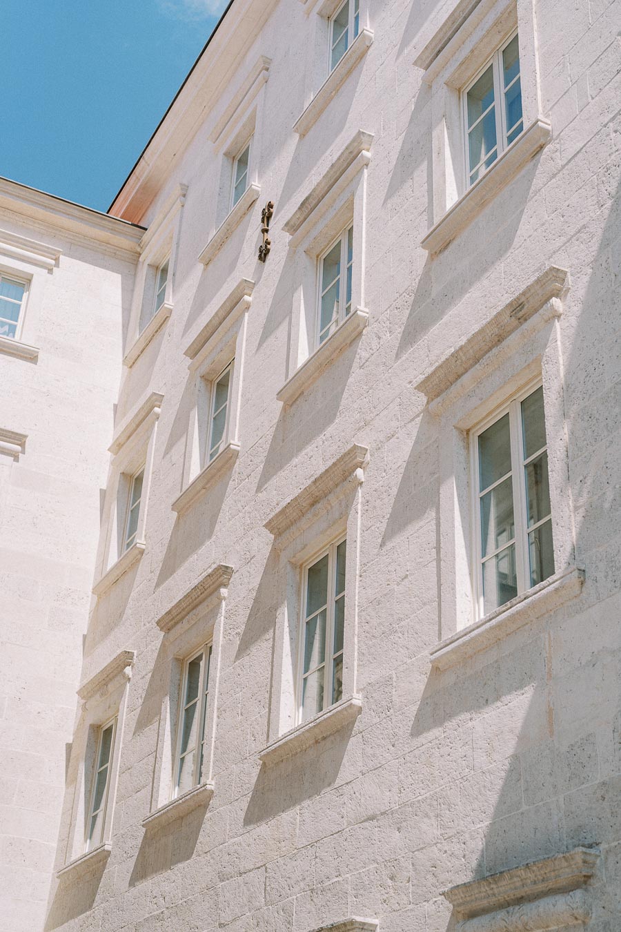 Exterior of a historic white stone building with multiple windows against a clear blue sky.