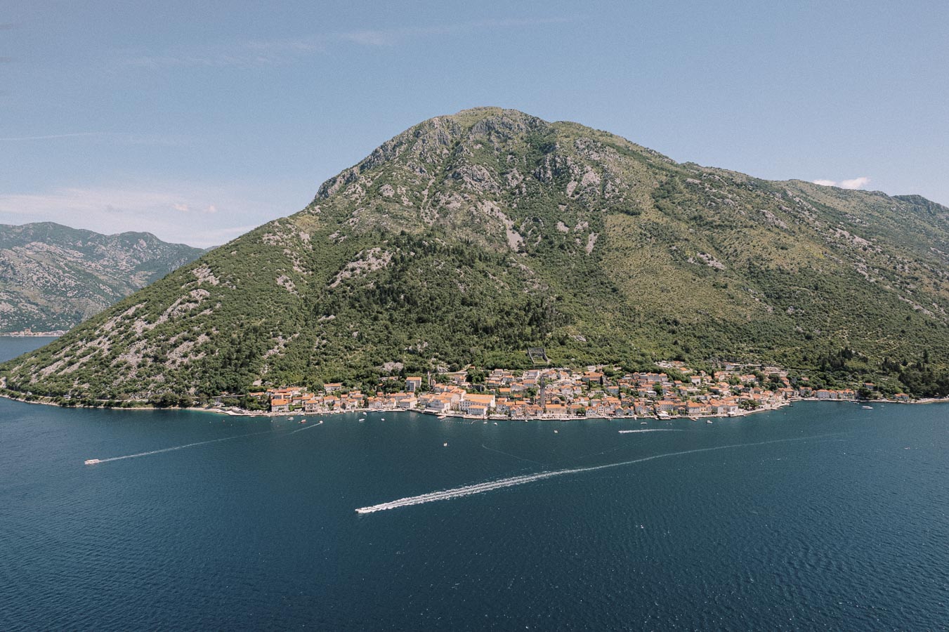 Aerial view of a coastal town nestled against a lush green mountain with a serene blue sea in the foreground, capturing the tranquil scenery of a Mediterranean landscape.