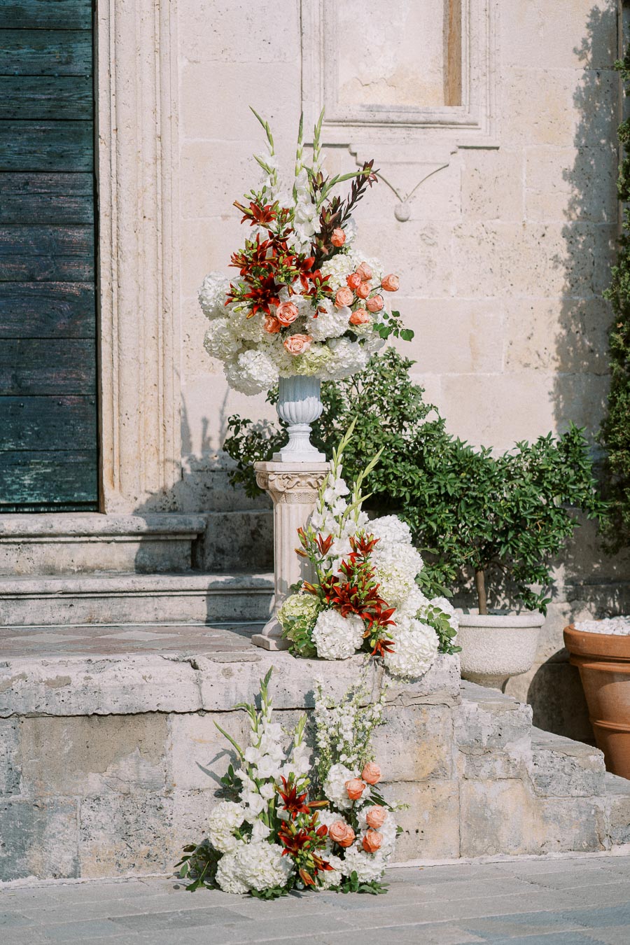 Elegant white and peach floral arrangements with lilies and roses on stone steps of a historic building, enhancing outdoor wedding decor.
