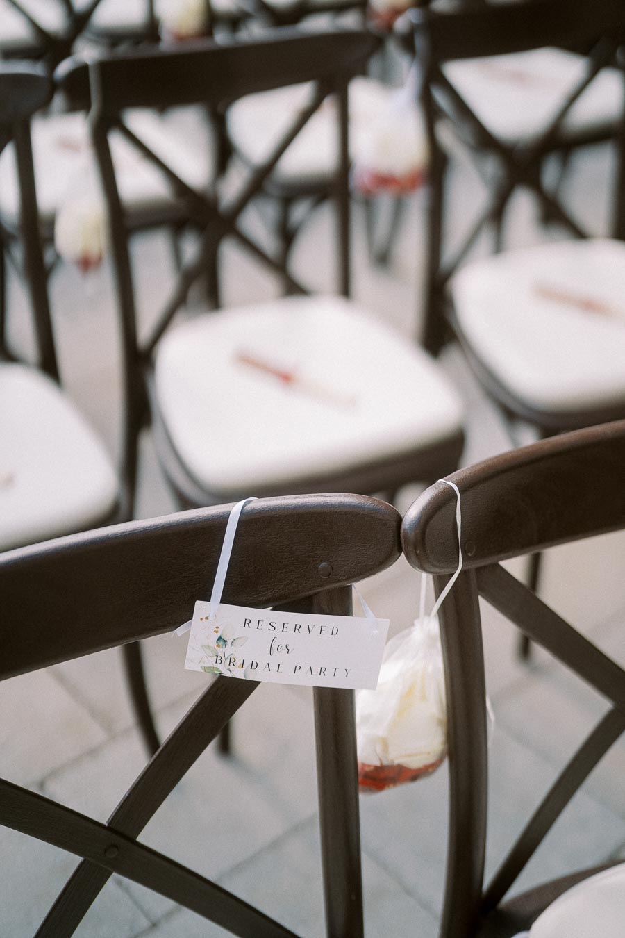 Elegant wooden chairs with white cushions arranged for an outdoor wedding ceremony, featuring a sign reading 'Reserved for Bridal Party' to designate seating.