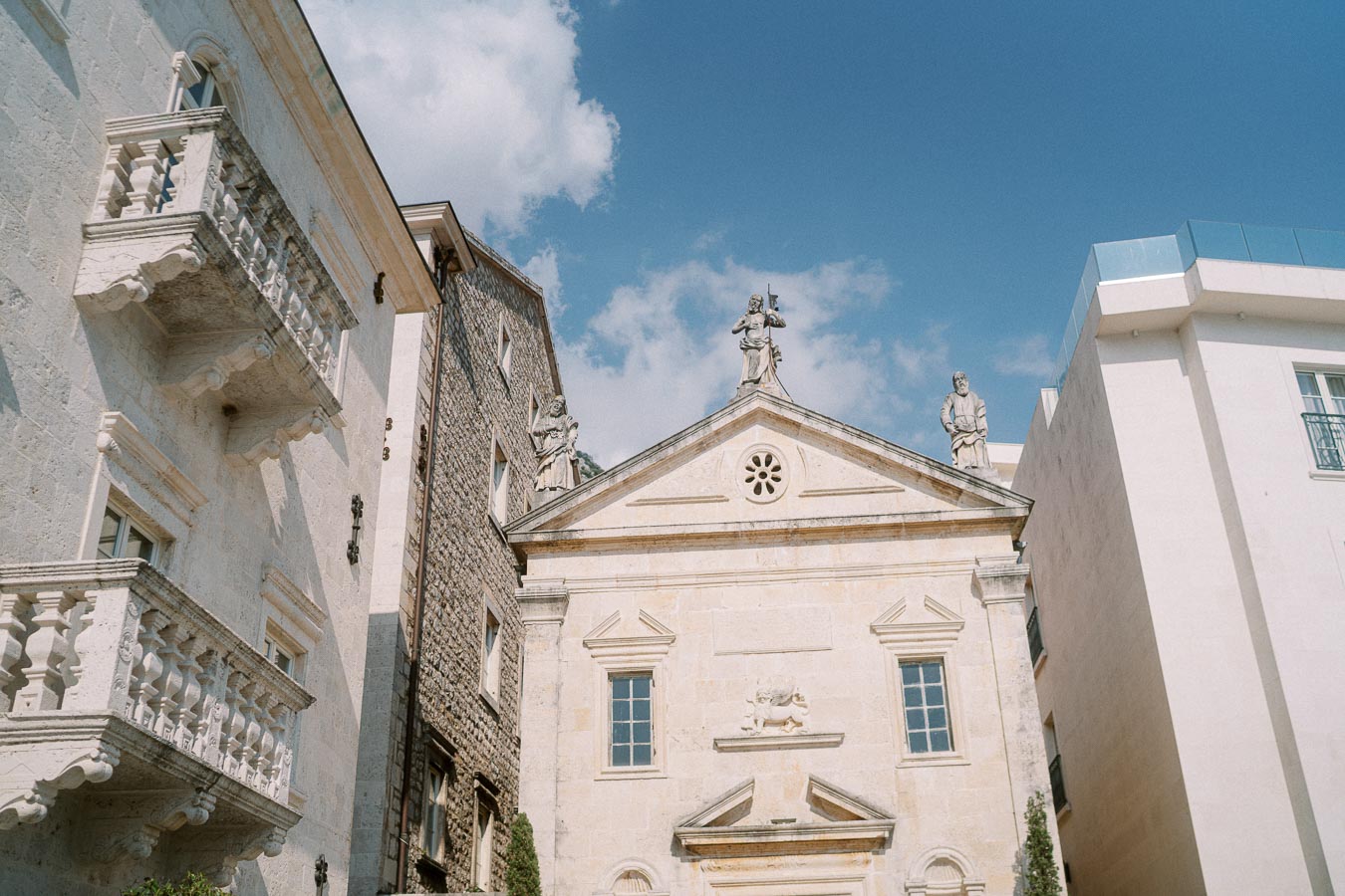 Historic European architecture with stone facade and statues under a blue sky, featuring elegant balconies and ancient detailing.