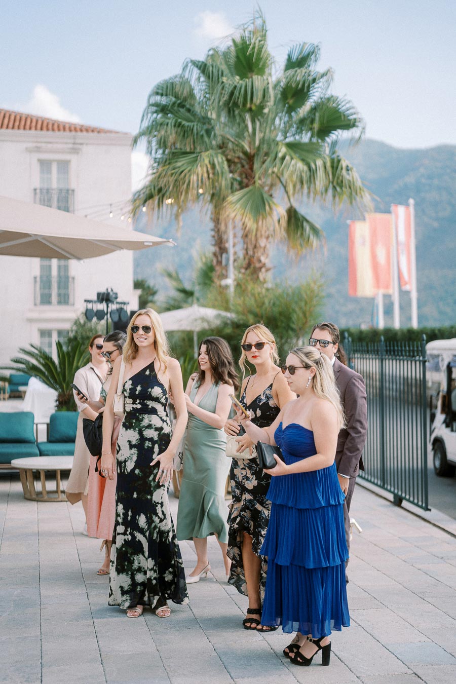 A group of stylishly dressed people enjoying an outdoor event with a backdrop of palm trees and mountains.