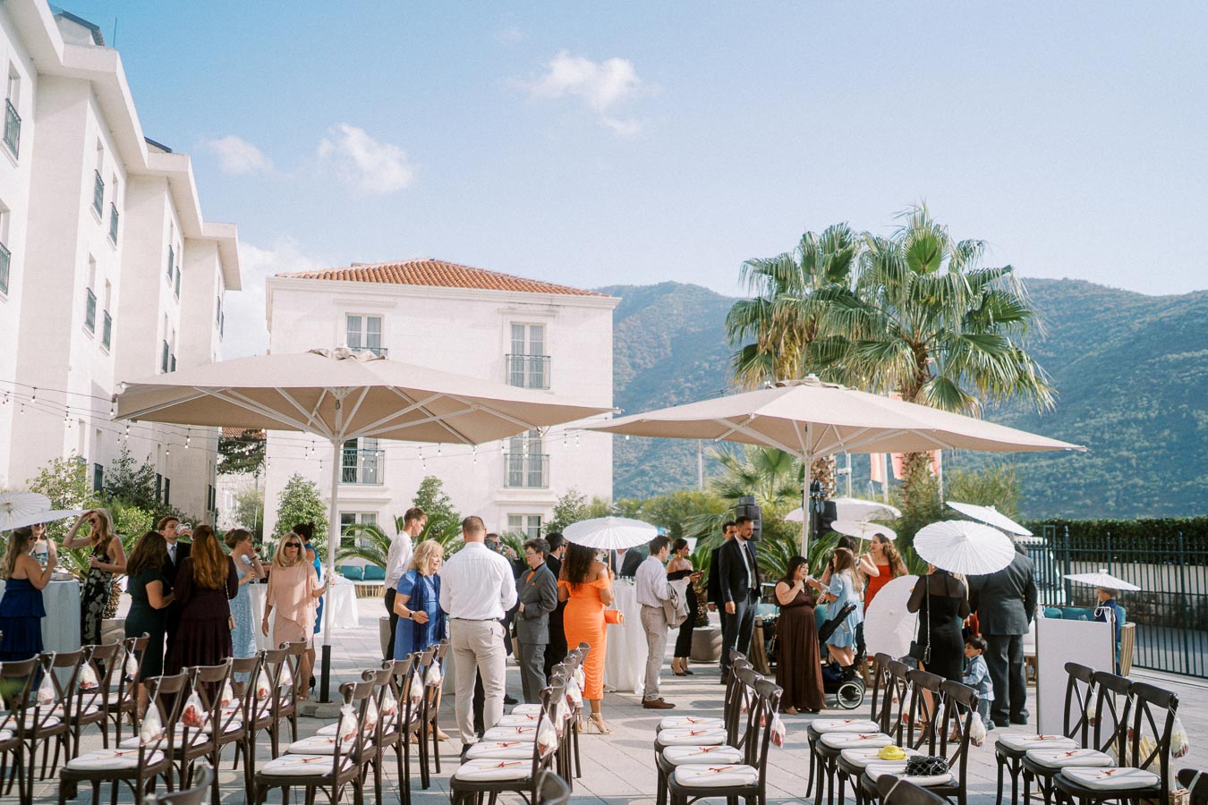 Outdoor wedding reception with guests mingling under large umbrellas, set against a scenic backdrop of mountains and palm trees.