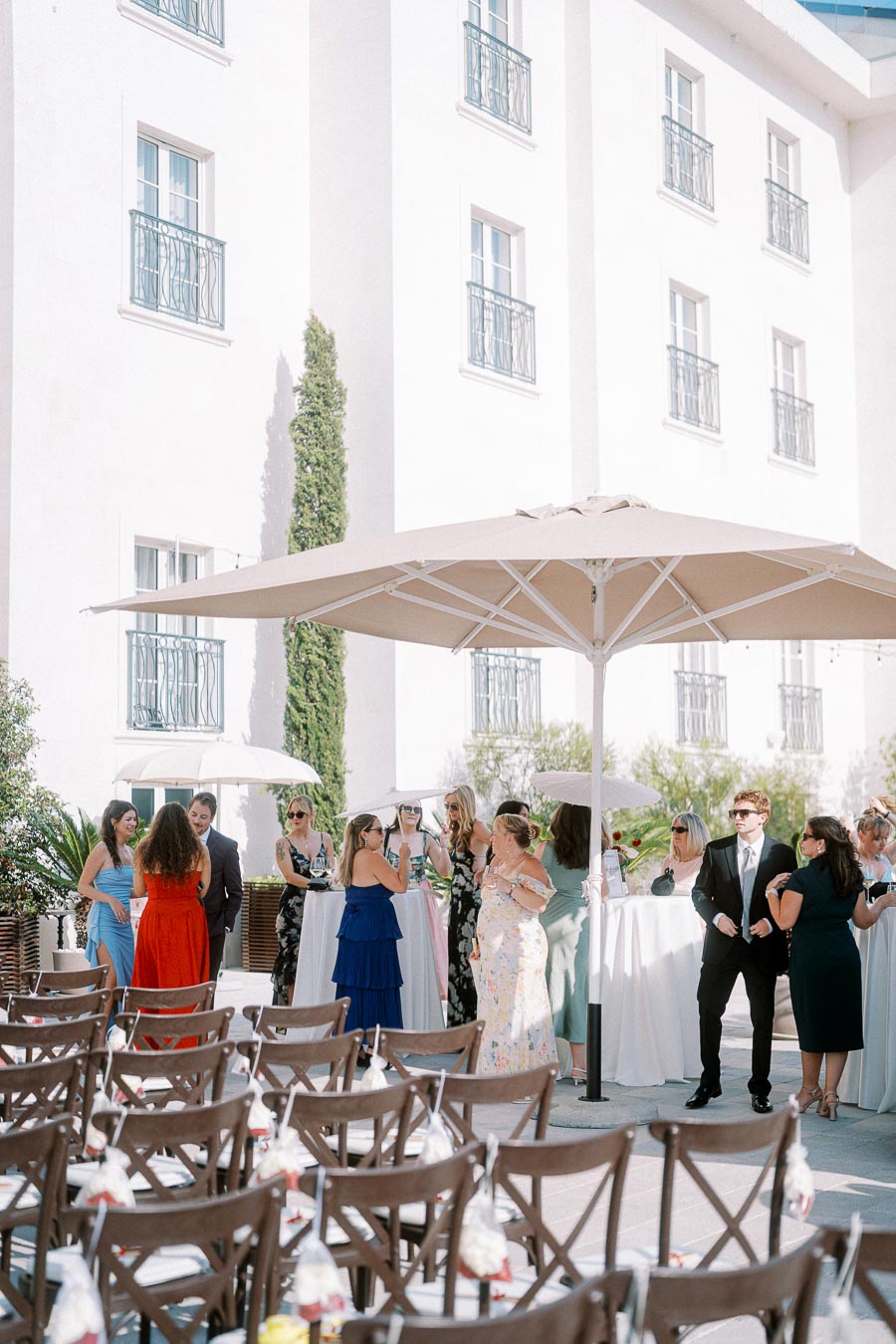 Outdoor wedding reception at a stylish venue with guests socializing under large umbrellas, surrounded by elegant decor and seating arrangements.