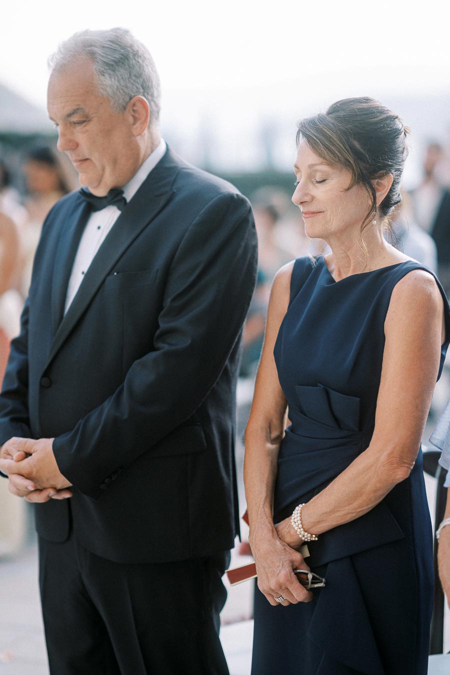 A couple dressed elegantly at a formal event, with the man wearing a suit and the woman in a blue dress, both appearing thoughtful and serene.
