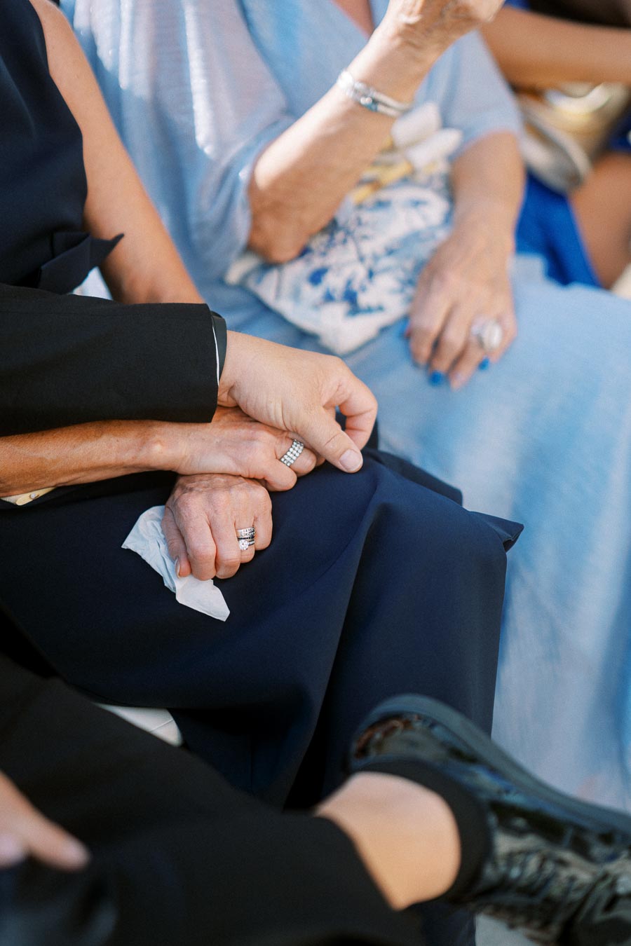 Couple holding hands tenderly, displaying silver rings and emotional warmth, with blue clothing in the background.