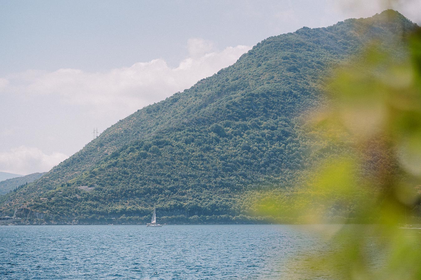 Peaceful sailboat on a tranquil blue sea with a lush green hillside in the background under a clear sky.