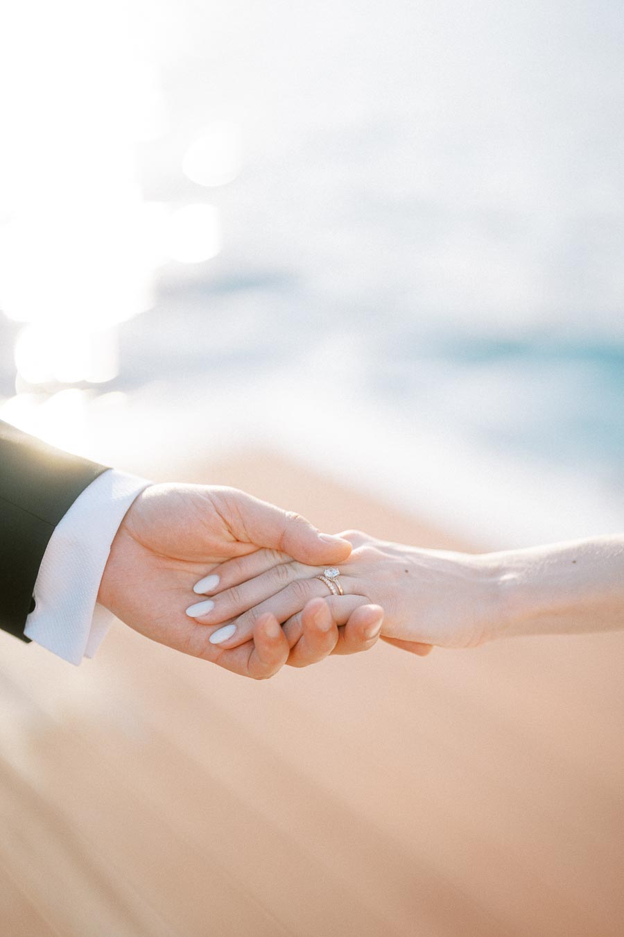Close-up of a couple holding hands, showcasing an engagement ring, with a soft romantic background, symbolizing love and commitment.