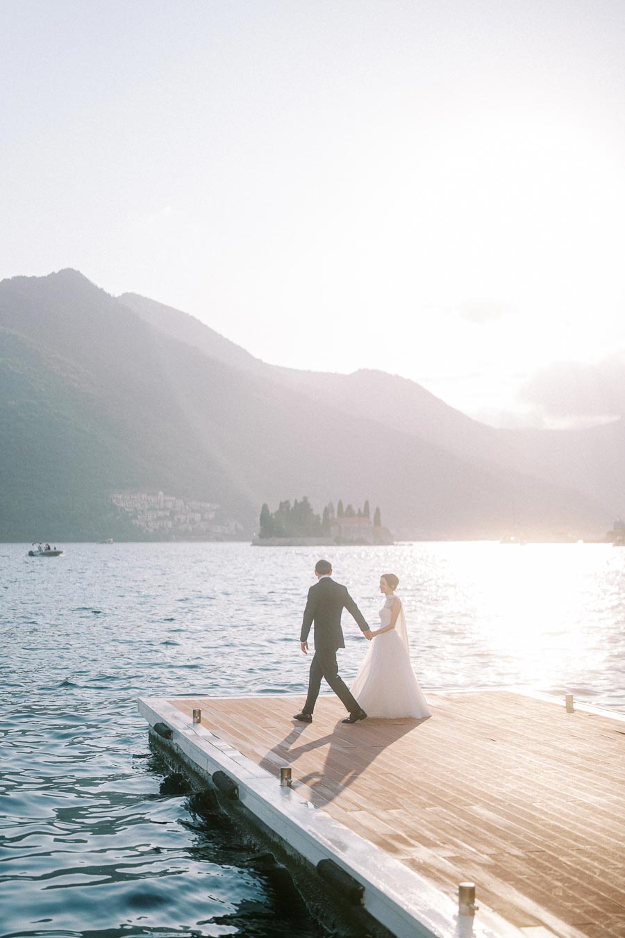 romantic wedding couple holding hands on a dock by a serene lake with mountain backdrop at sunset