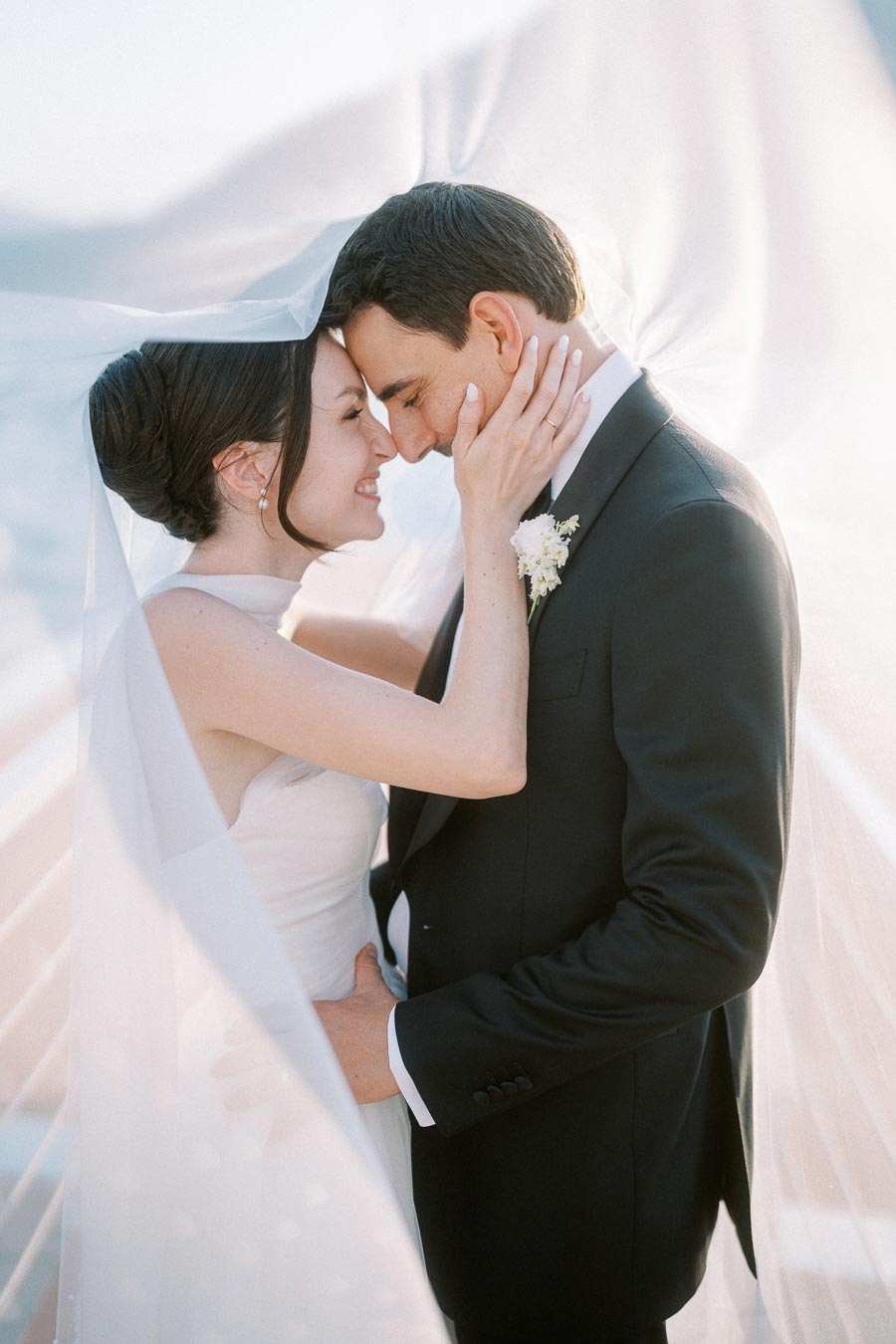 Romantic bride and groom embracing under a flowing veil during a wedding photoshoot.