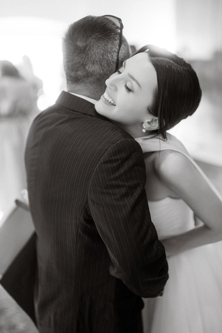 A joyful bride hugging a man in a suit, captured in a candid moment during a wedding celebration.