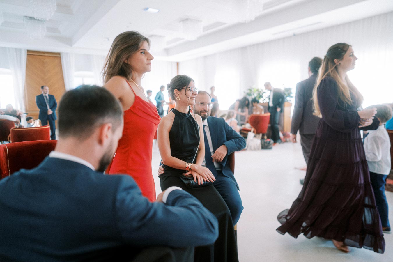 Group of elegantly dressed people socializing in a well-lit indoor setting, featuring stylish clothing and a relaxed atmosphere.