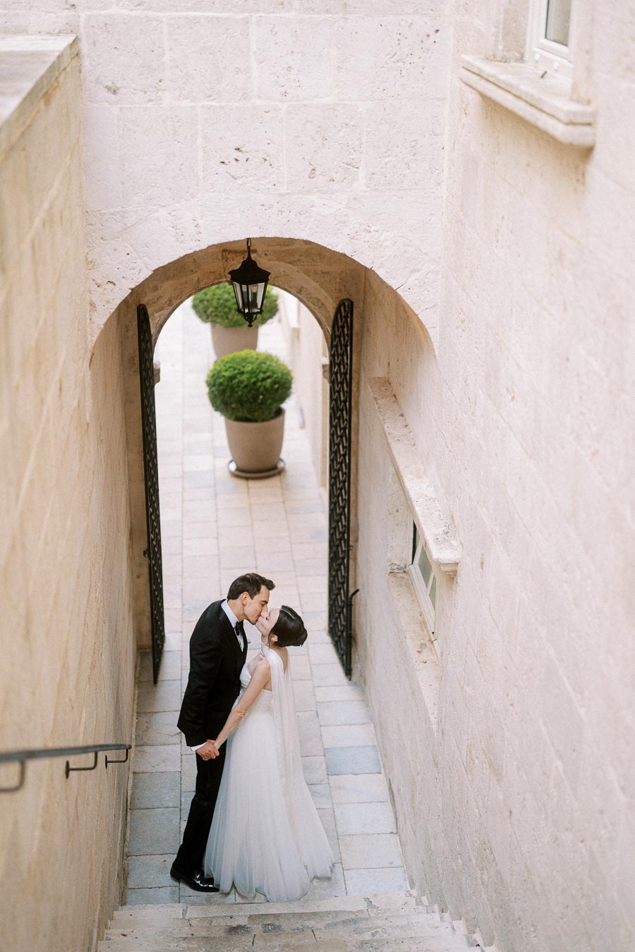Elegant wedding couple sharing a romantic kiss in picturesque stone archway setting.