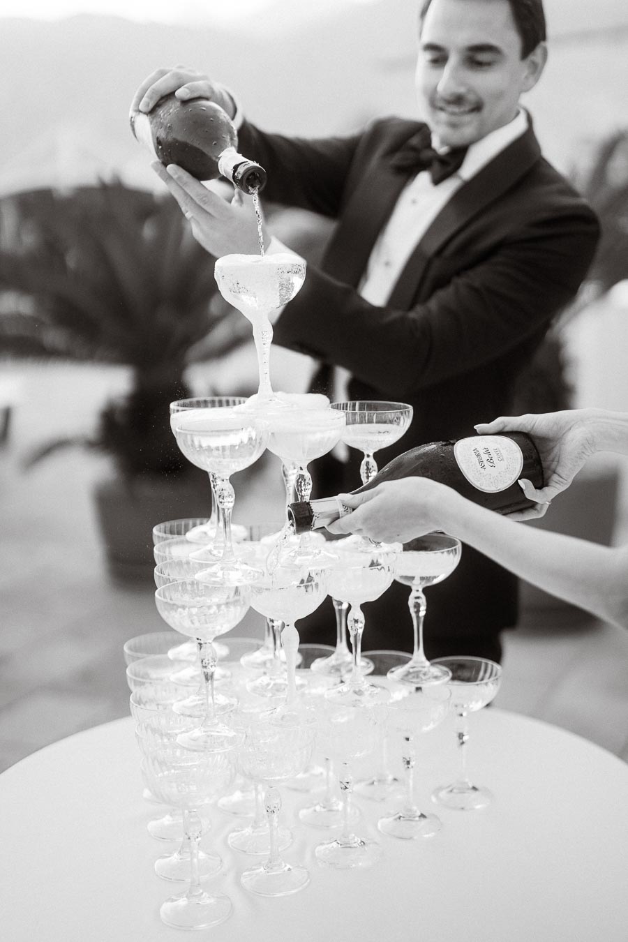 A man in a tuxedo pouring champagne into a cascading tower of glasses at an elegant event, creating a luxurious and celebratory atmosphere.