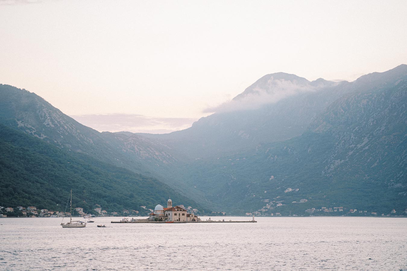 Peaceful landscape of a serene bay with a small island church, surrounded by green mountains and calm waters, perfect for travel and nature enthusiasts exploring coastal scenery.