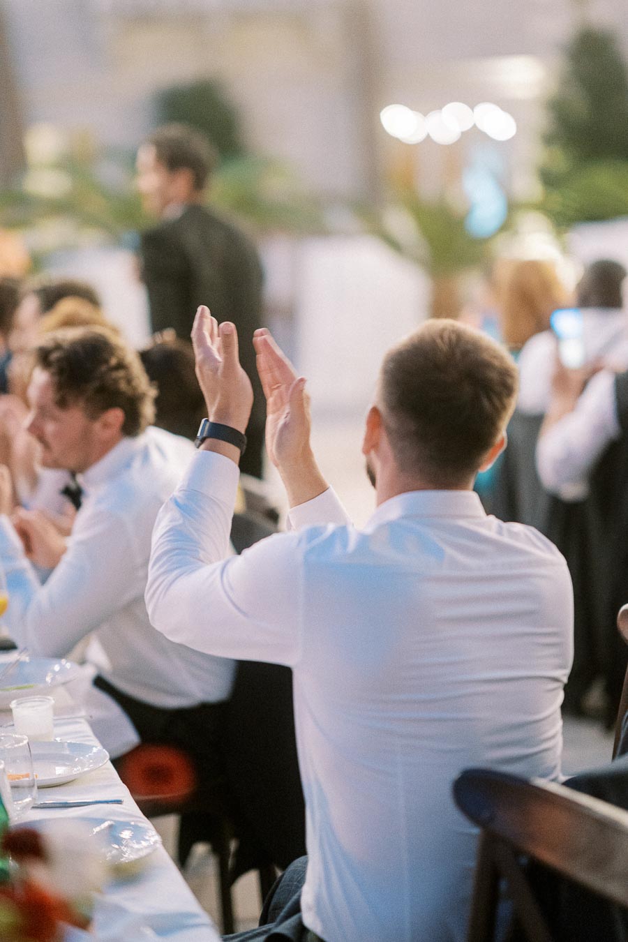 People clapping at a formal event, seated at a banquet table with elegant white attire, indicating celebration or appreciation.