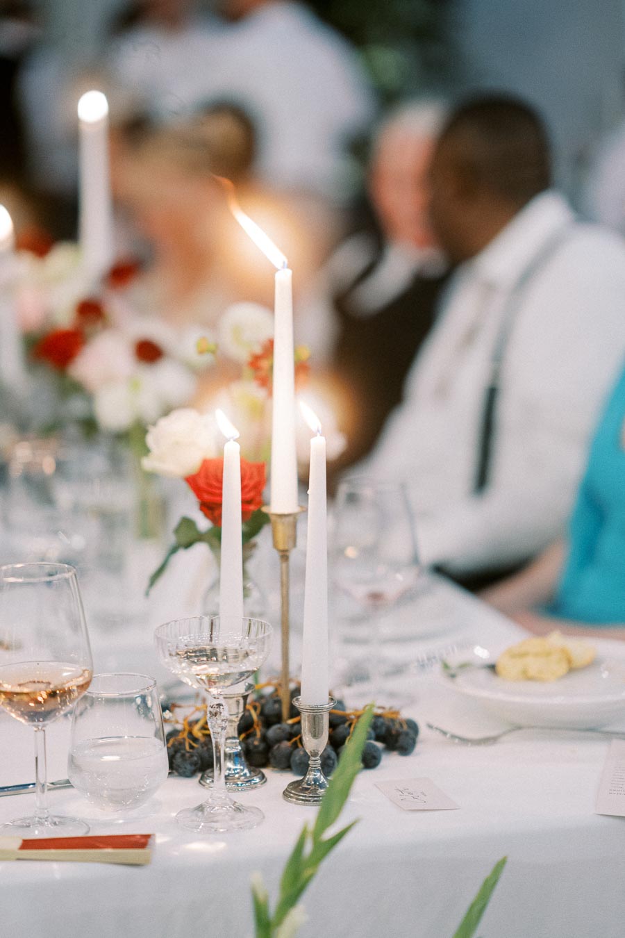 Elegant wedding table setting with lit candles, rose centerpiece, wine glasses, and plates.