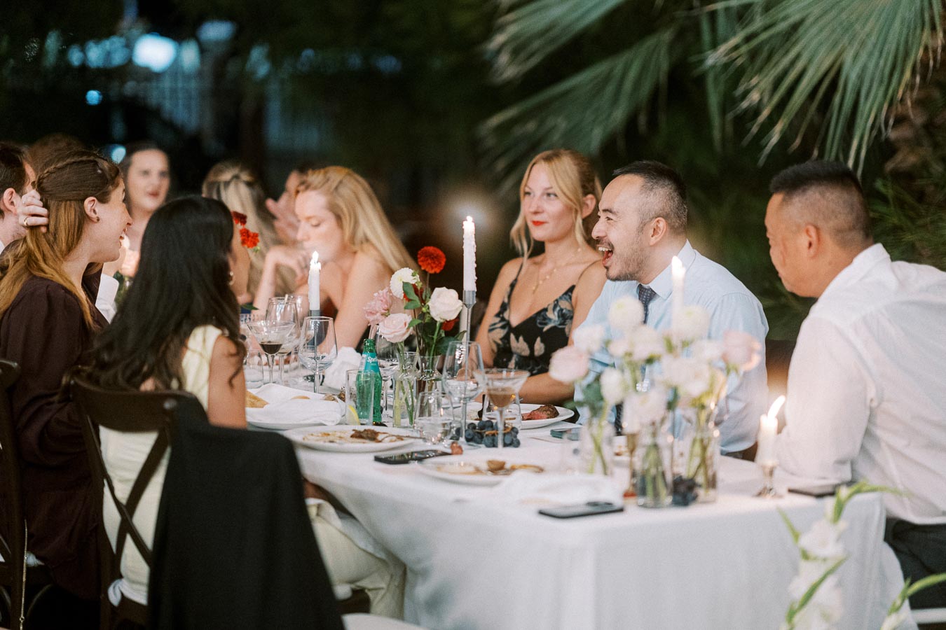 A group of people enjoying an elegant outdoor dinner party at night, with a beautifully set table adorned with flowers and candles.