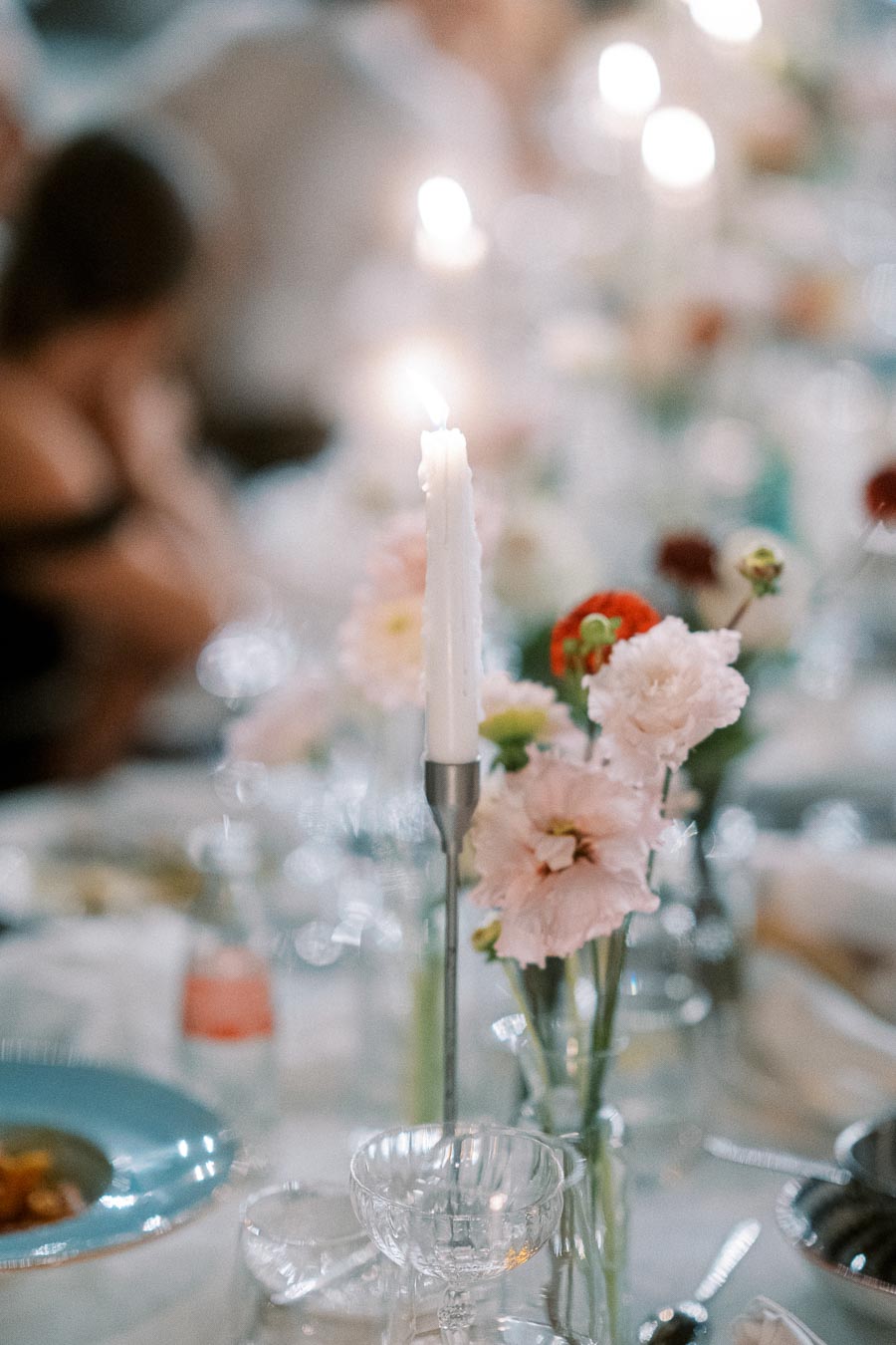 Elegant dinner table setting with a lit candle surrounded by delicate pink and red flowers, creating a romantic and intimate atmosphere.